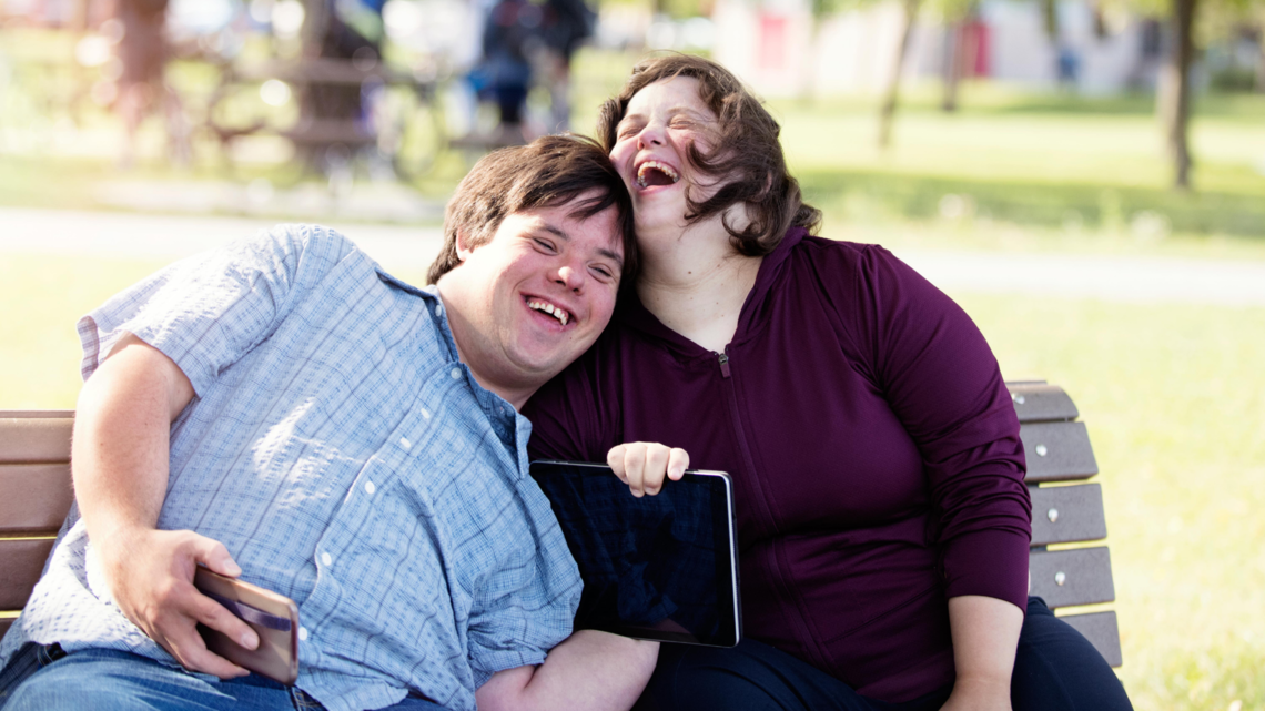 Photo of two adults sitting on a bench smiling